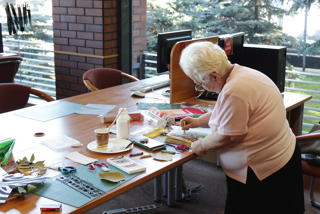  Uczestniczka warsztatów w trakcie pracy ozdabiania książki stoi przy stole na którym znajdują się materiały plastyczne i artystyczne.