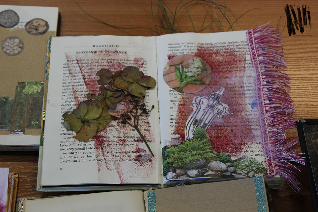 Otwarta książka z naklejonymi ususzonymi kwiatami, wycinkami z gazet i listwą z frędzlami.