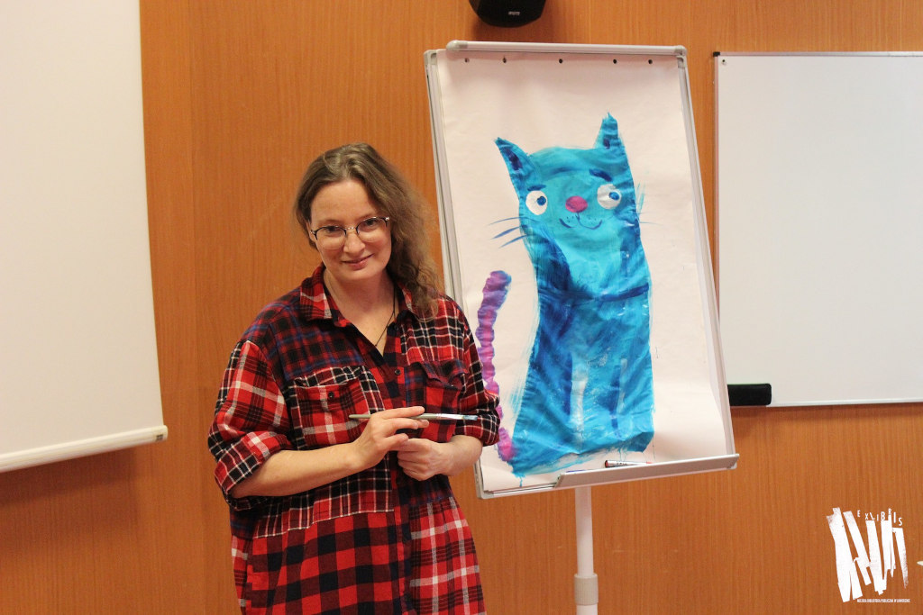 Katarzyna Kołodziej stoi przy namalowanej przez siebie postaci niebieskiego kotka.