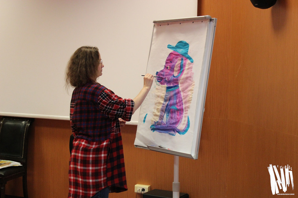 Audytorium Miejskiej Biblioteki Publicznej w Jaworznie, Katarzyna Kołodziej maluje postać różowego pieska na białej kartce tablicy flibchart.