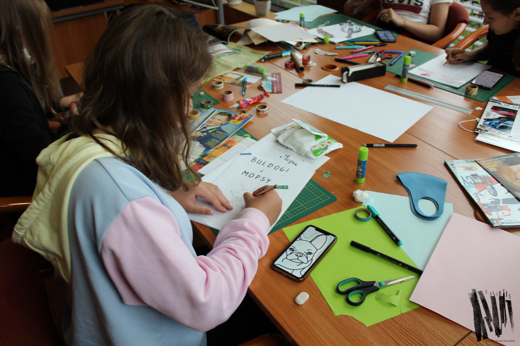 Uczestnicy warsztatów podczas pracy: rysowanie ołówkami, wokół rozłożone na stole gazety i materiały plastyczne.