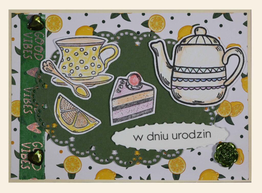 Ozdobna kartka, motywy: owoce cytrusowe, filiżanka, dzbanek, ciastko - torcik, obok napis: „w dniu urodzin”.