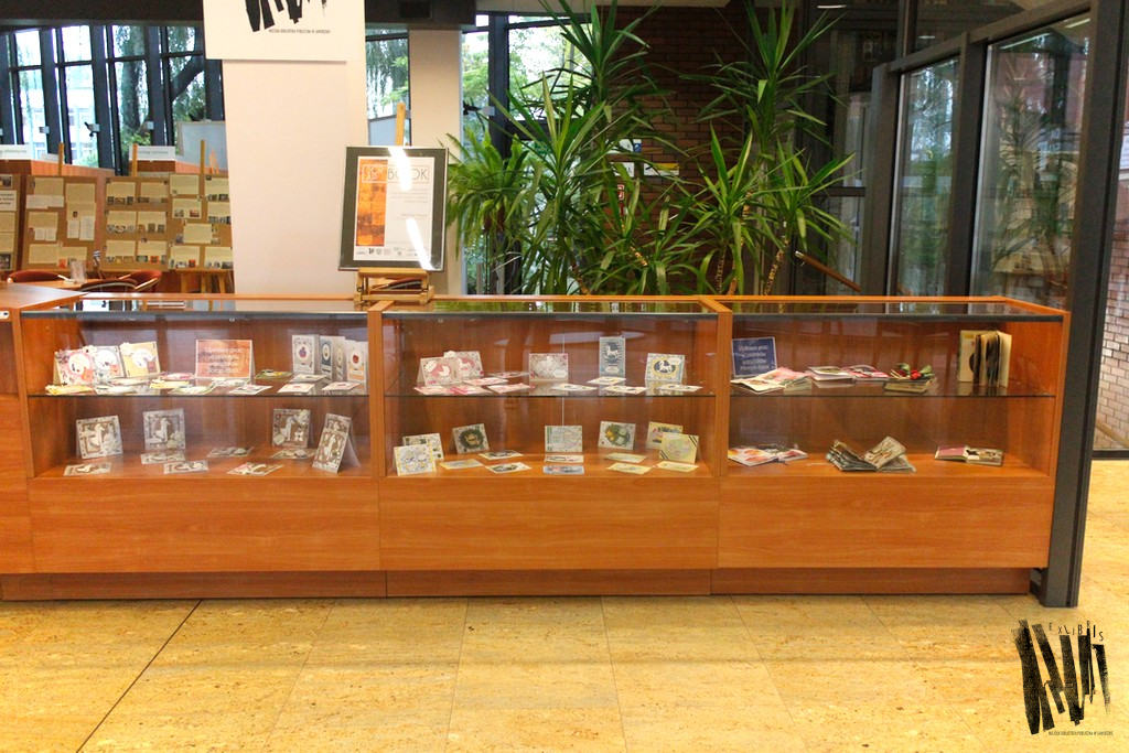 Hol Biblioteki Głównej widok na wystawę - przeszklone gabloty, w których prezentowane są prace uczestników warsztatów.
