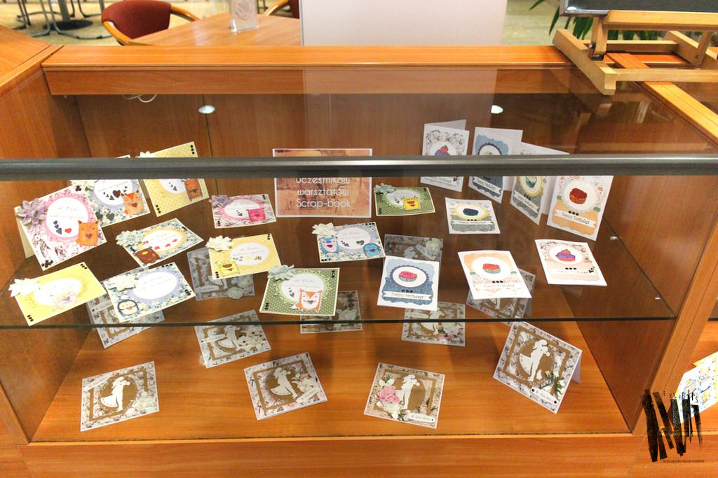 Przeszklona gablota, w niej prezentowane kartki artystyczne podpis: Wystawa prac uczestników warsztatów scrap-book